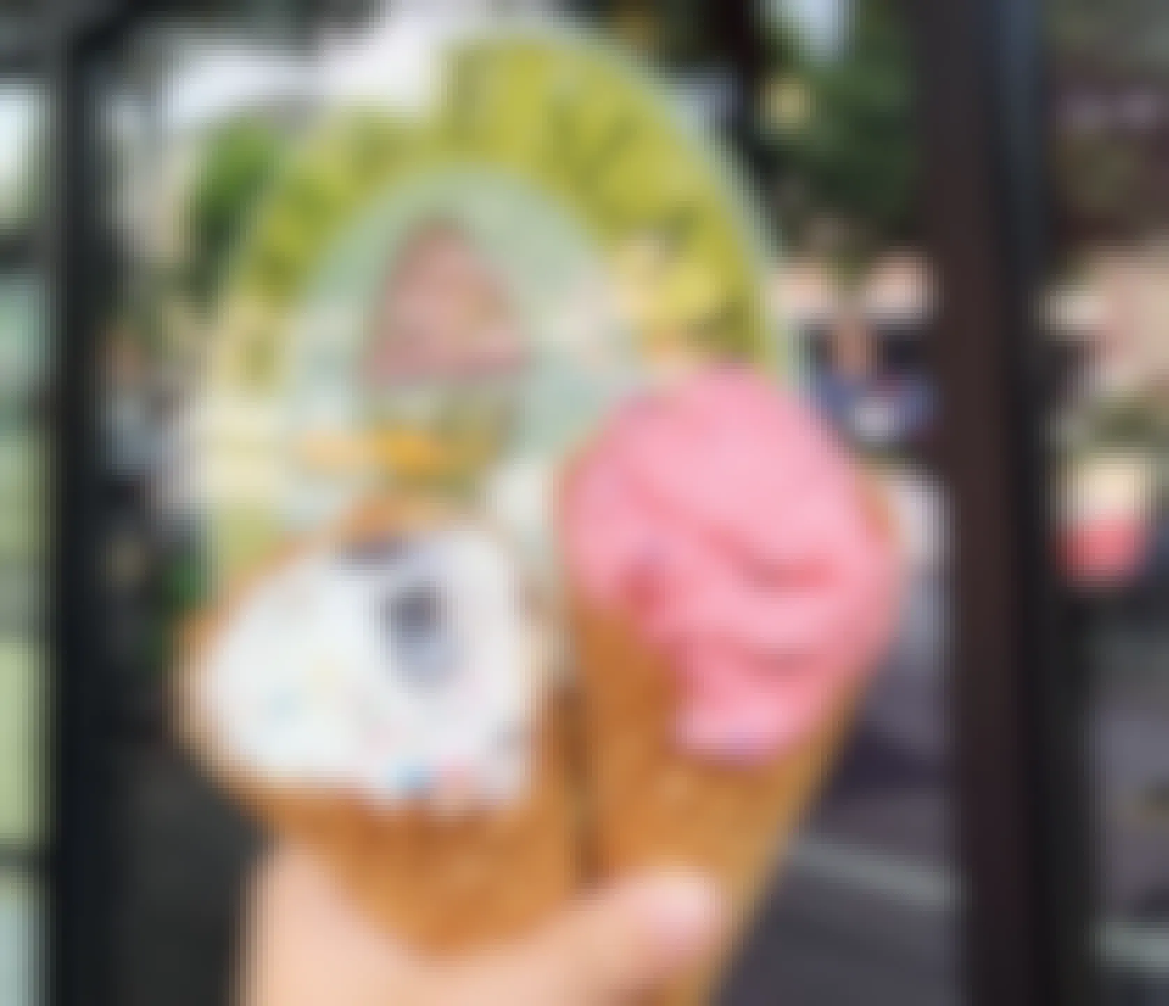 person holding ice cream waffle cones in front of marble slab creamery sign