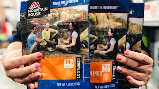 A person's hand holding up three Mountain House pouches.