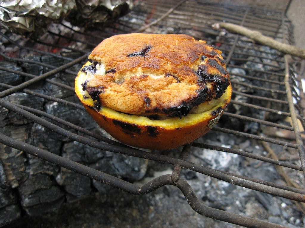 Blueberry muffins being baked over a campfire in a halved orange