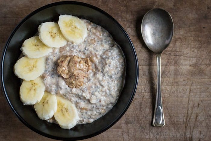 Oatmeal in a bowl with peanut butter and sliced banana next to a silver spoon.