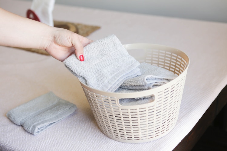 A person sorting wash clothes into a dollar tree plastic basket.