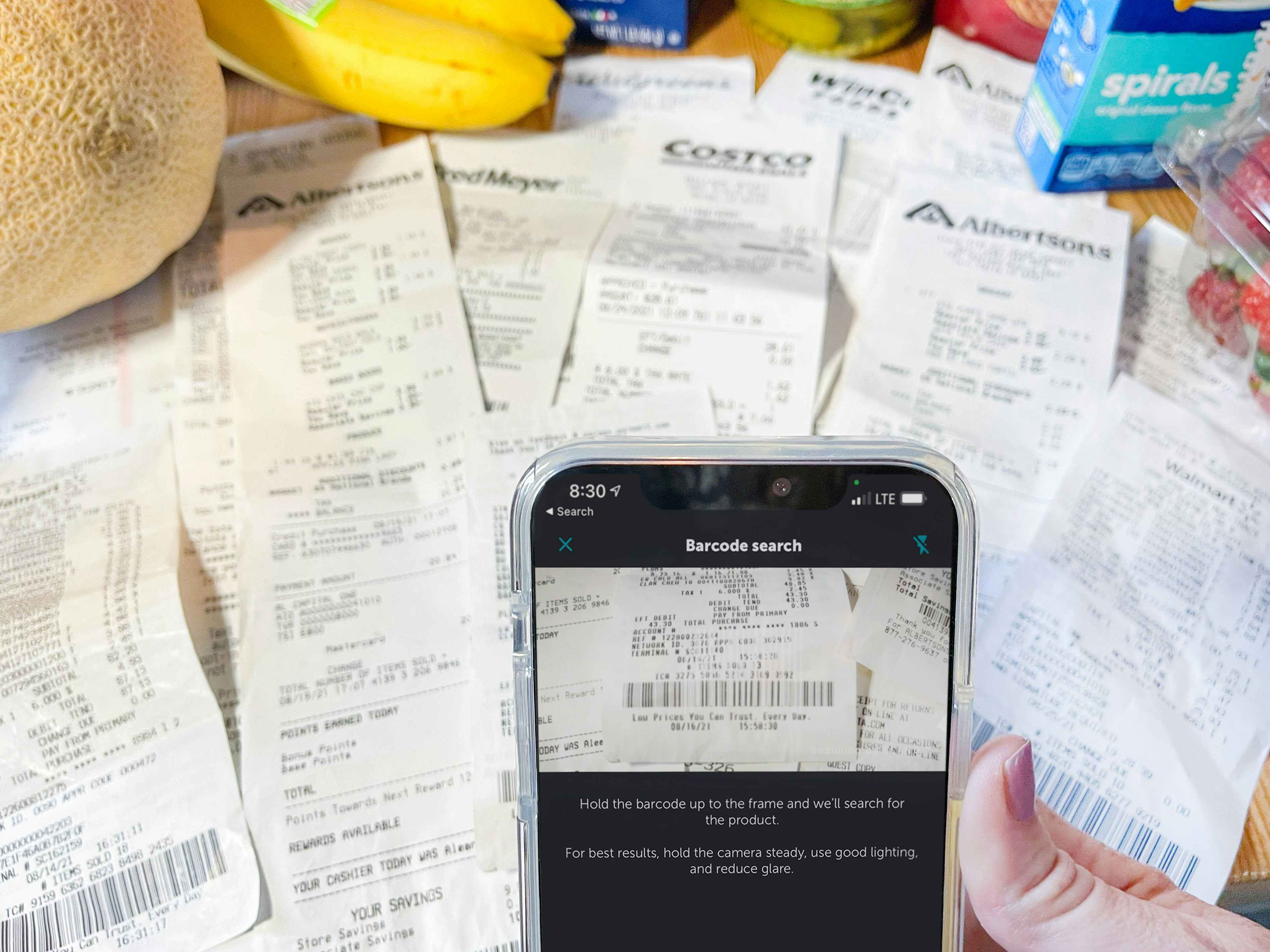 cellphone being held with app in front of groceries and other receipts