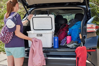 A person opening a yeti cooler in the trunk of their suv