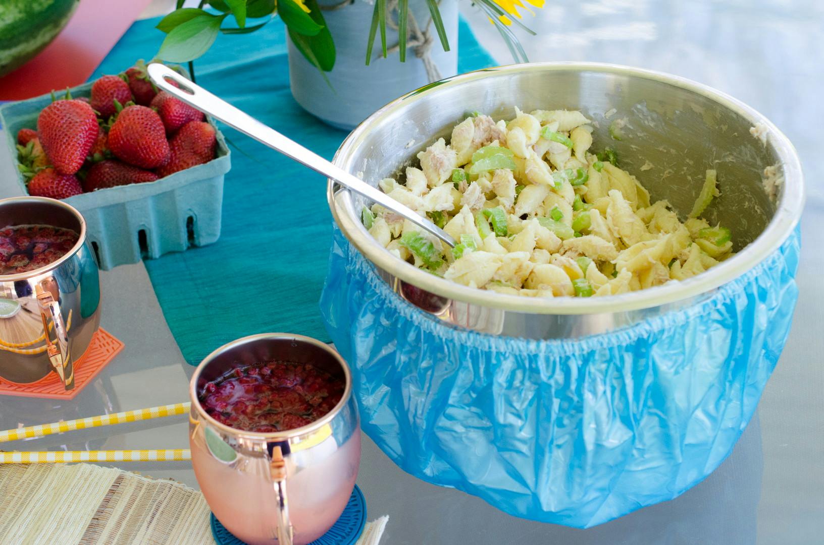 A pasta salad in a metal bowl with a shower cap around it.