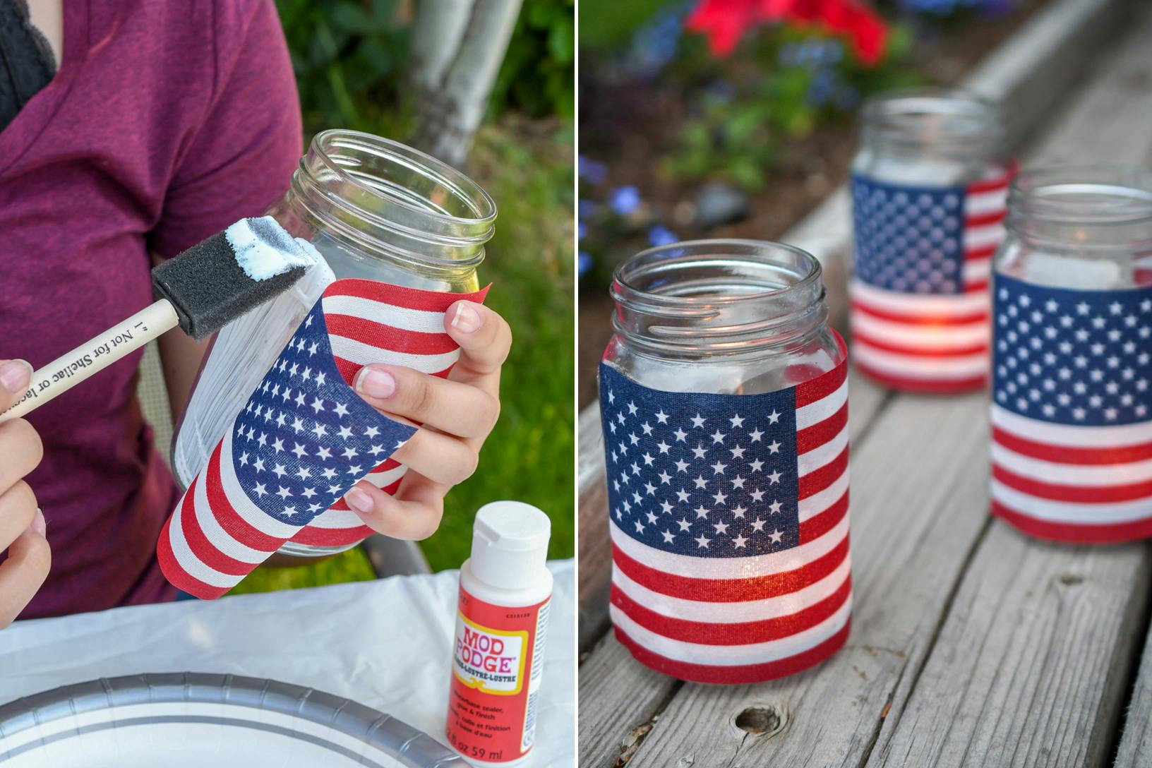 A person painting Mod Podge onto a mason jar and sticking an American flag to the side next to three completed jars with lights inside, making 4th of July American flag lighting.