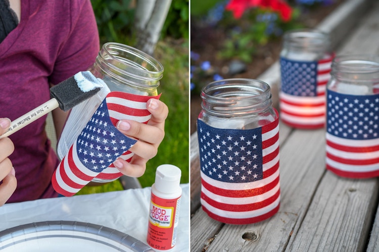 A person painting Mod Podge onto a mason jar and sticking an American flag to the side next to three completed jars with lights inside, making 4th of July American flag lighting.