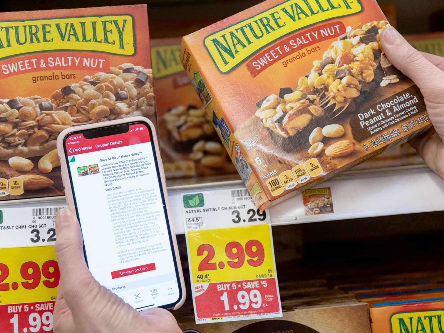 A person holding a phone with kroger app open near a box of granola bars the app has a coupon for