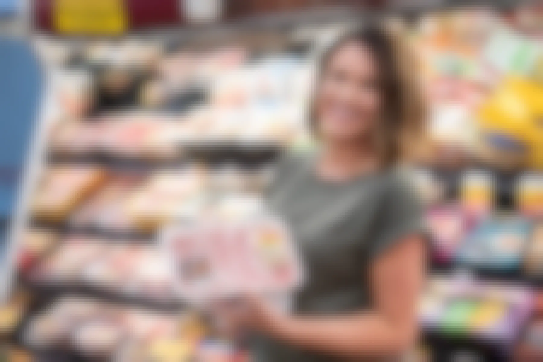 A woman smiling while holding up a few packages of pork chops in a grocery store.