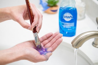woman cleaning a paint brush over a sink with Dawn dish soap nearby