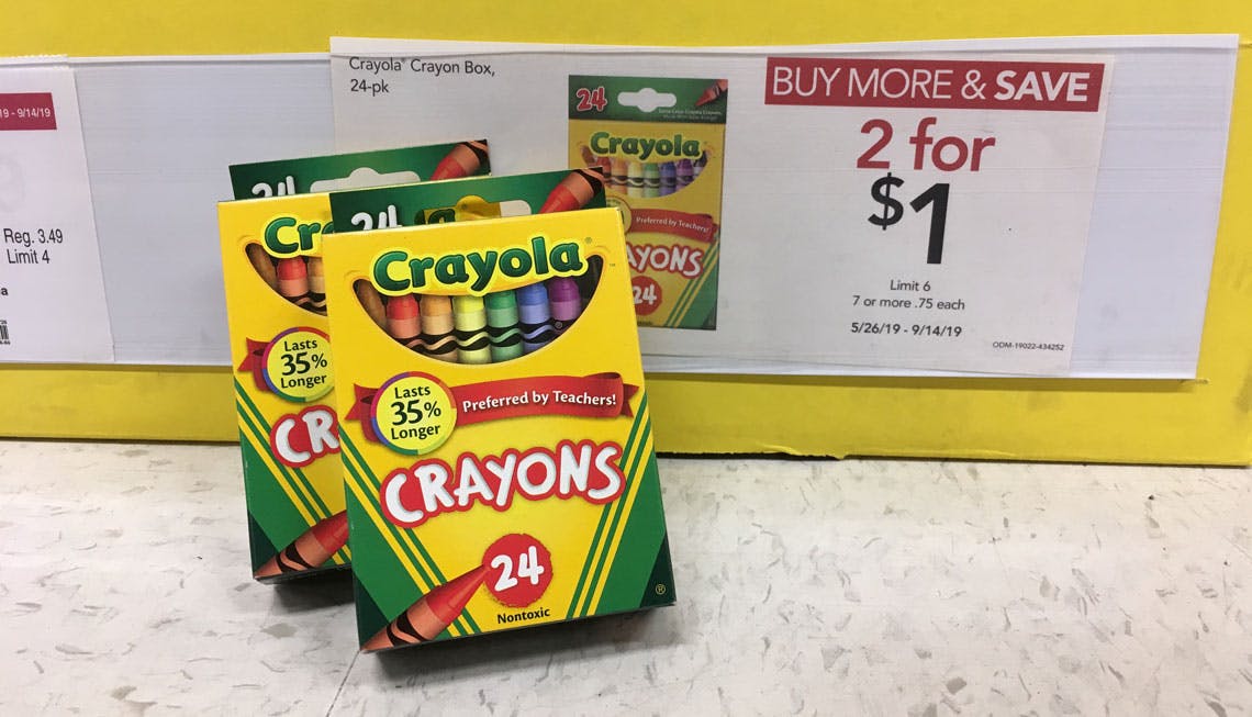 Two packs of Crayola 24-count crayons leaning up against a sale tag advertising a 2 for $1 sale at Office Depot.