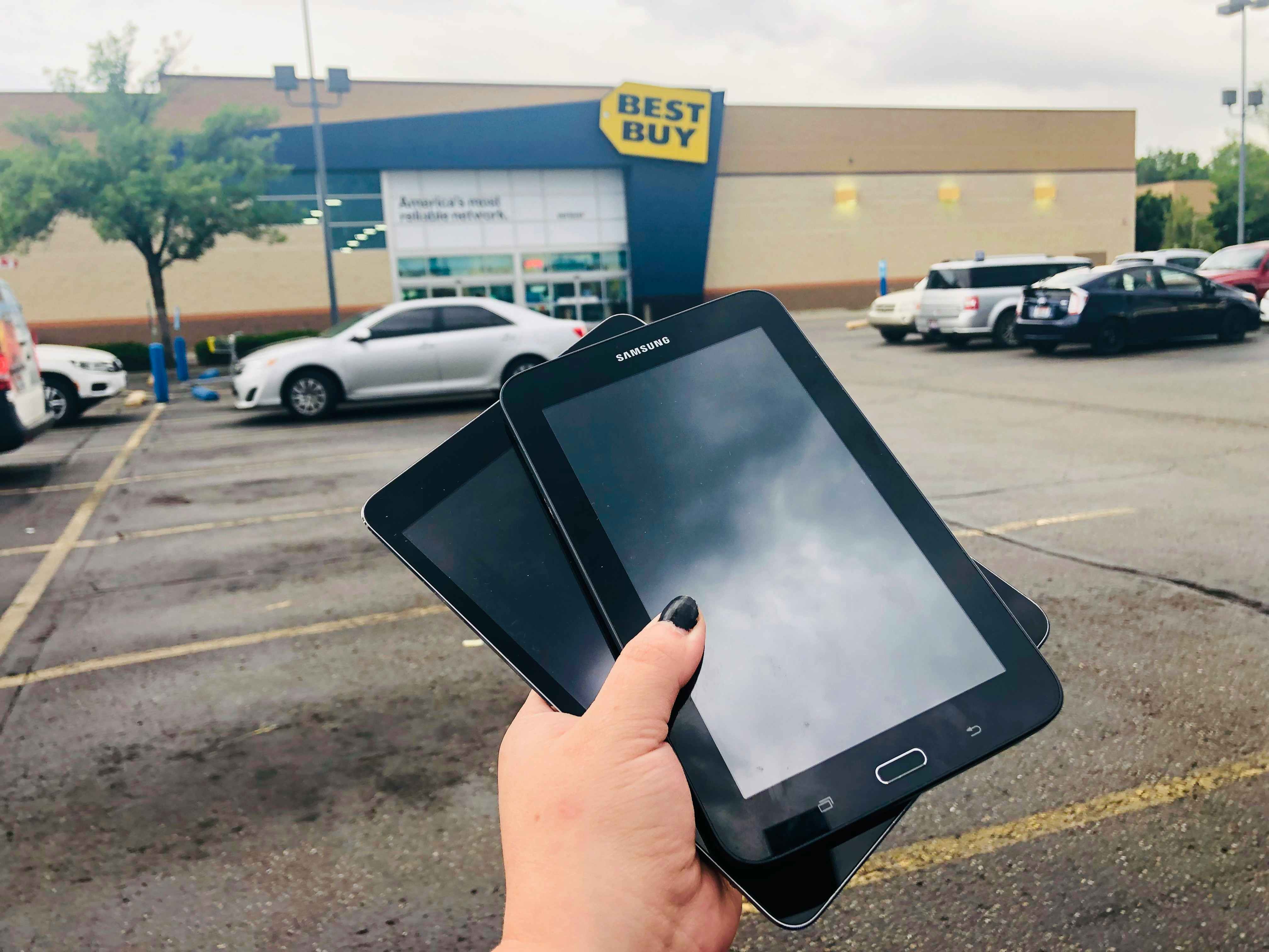 hand holds two older samsung tablets to trade in, in front of a best buy store