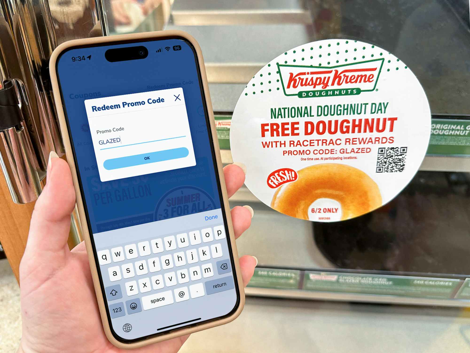 Someone holding a phone next to the RaceTrac Krispy Kreme donut display with a sign advertising the National Doughnut Day offer with the promo code GLAZED