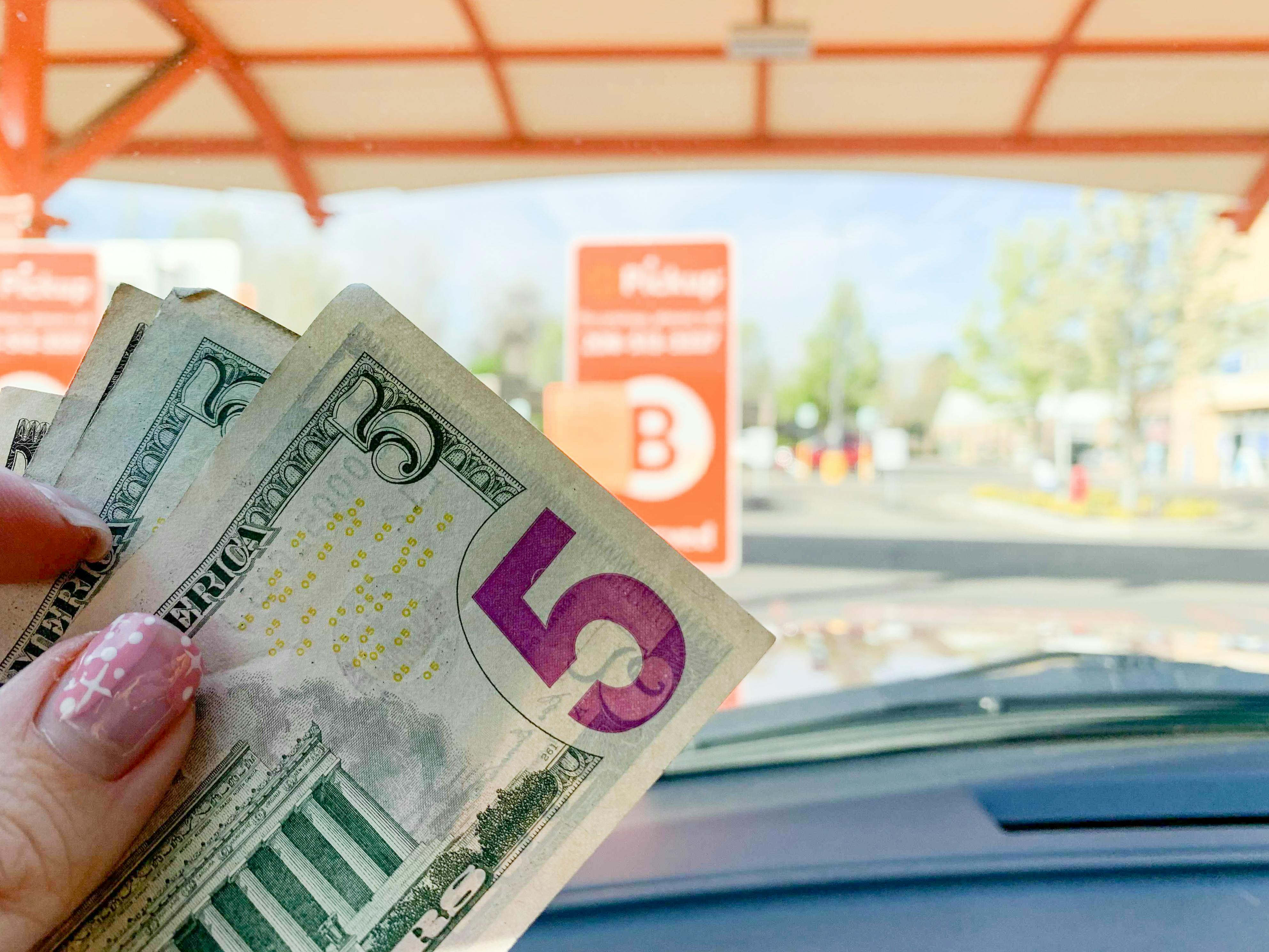 A person holding two $5 bills in front of a grocery pickup sign at Walmart.