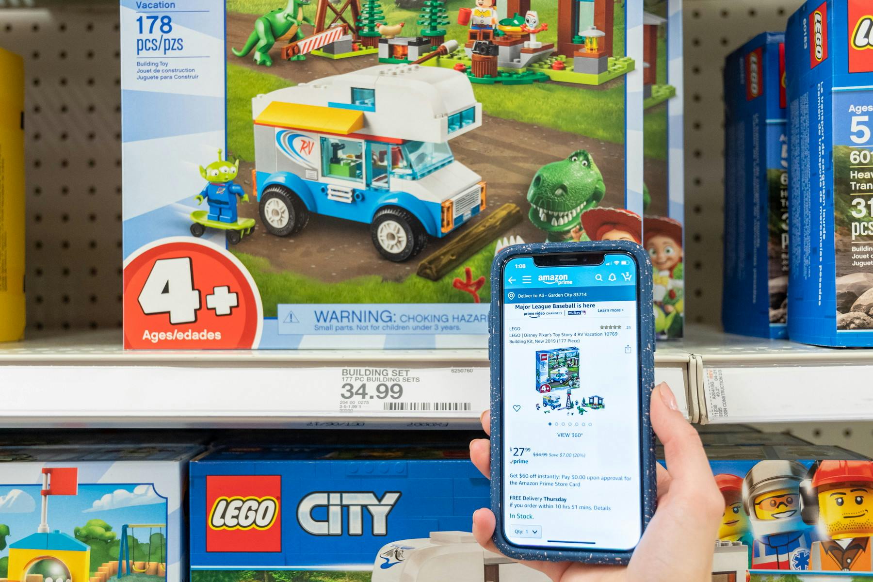 A person's hand holding up their phone displaying a product on the Amazon app in front of the physical product sitting on a Target shelf.