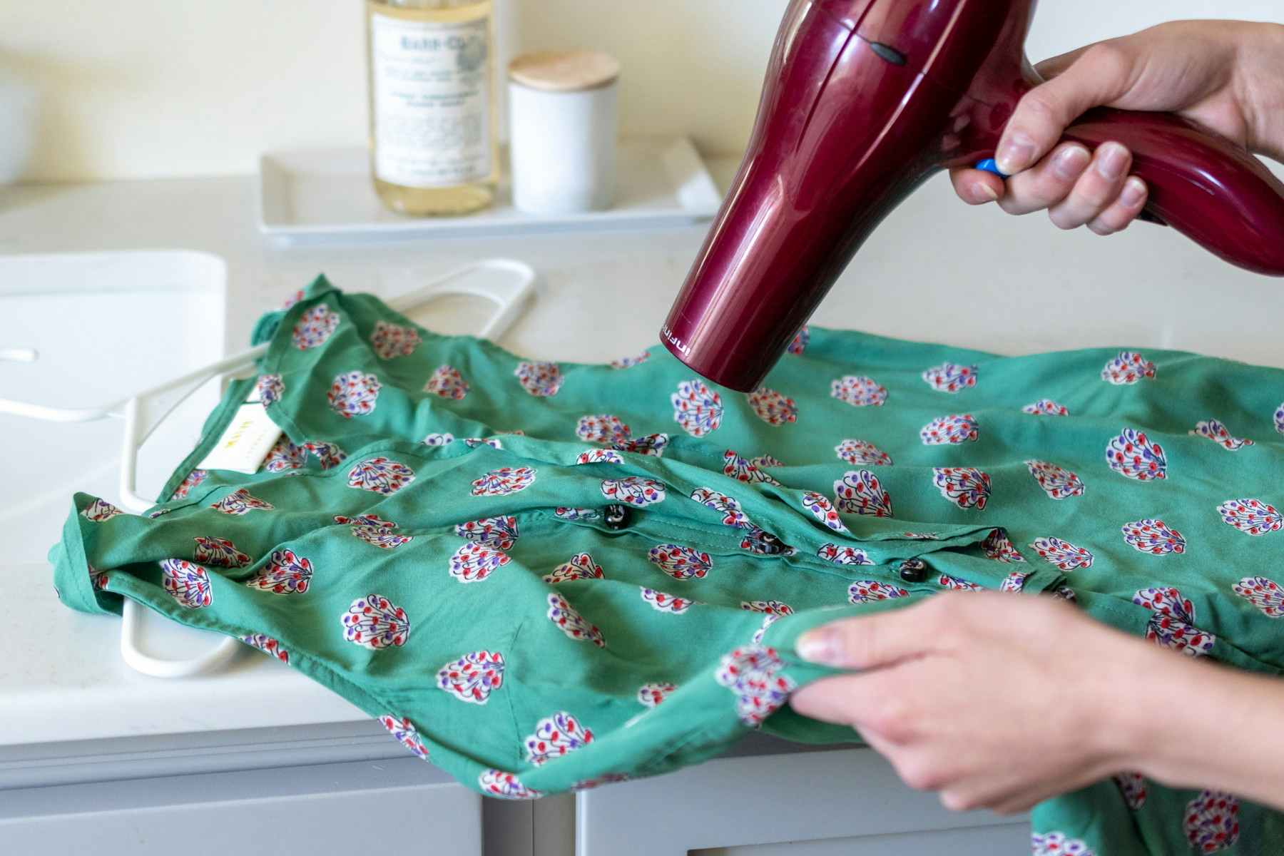 A blow dryer being pointed to the wrinkled areas of a shirt