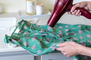 A blow dryer being pointed to the wrinkled areas of a shirt