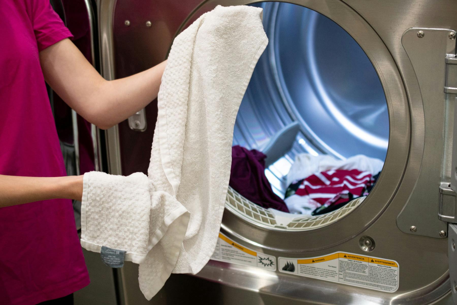 Woman holding a wrinkled towel in front of an open clothes dryer.