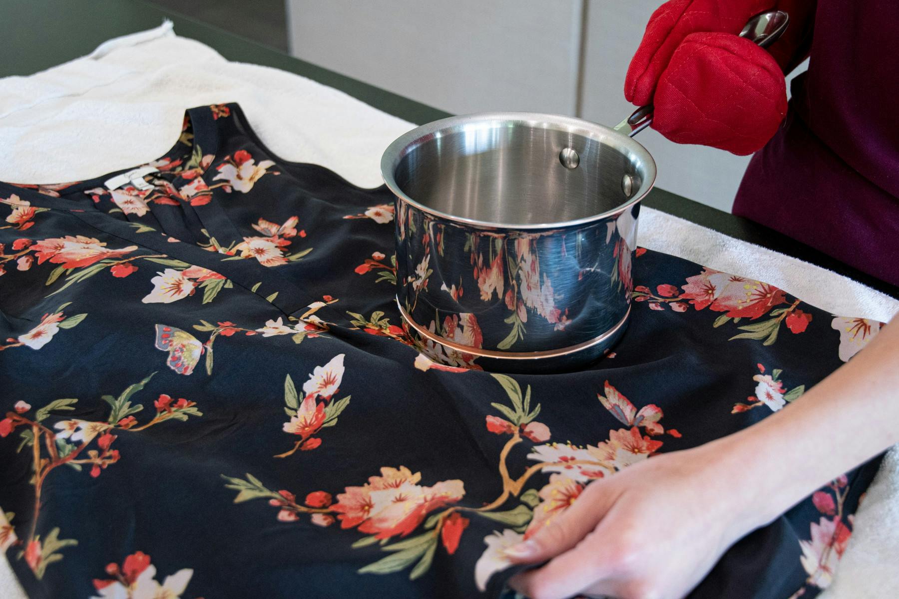A hot pot being held over a wrinkled shirt.