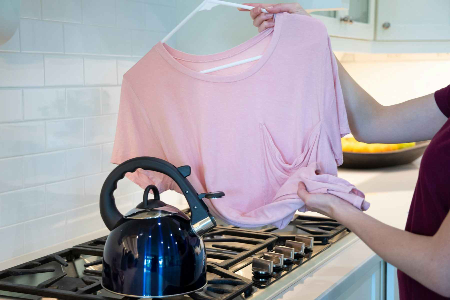 Woman holding a wrinkled shirt over the steam from a tea kettle