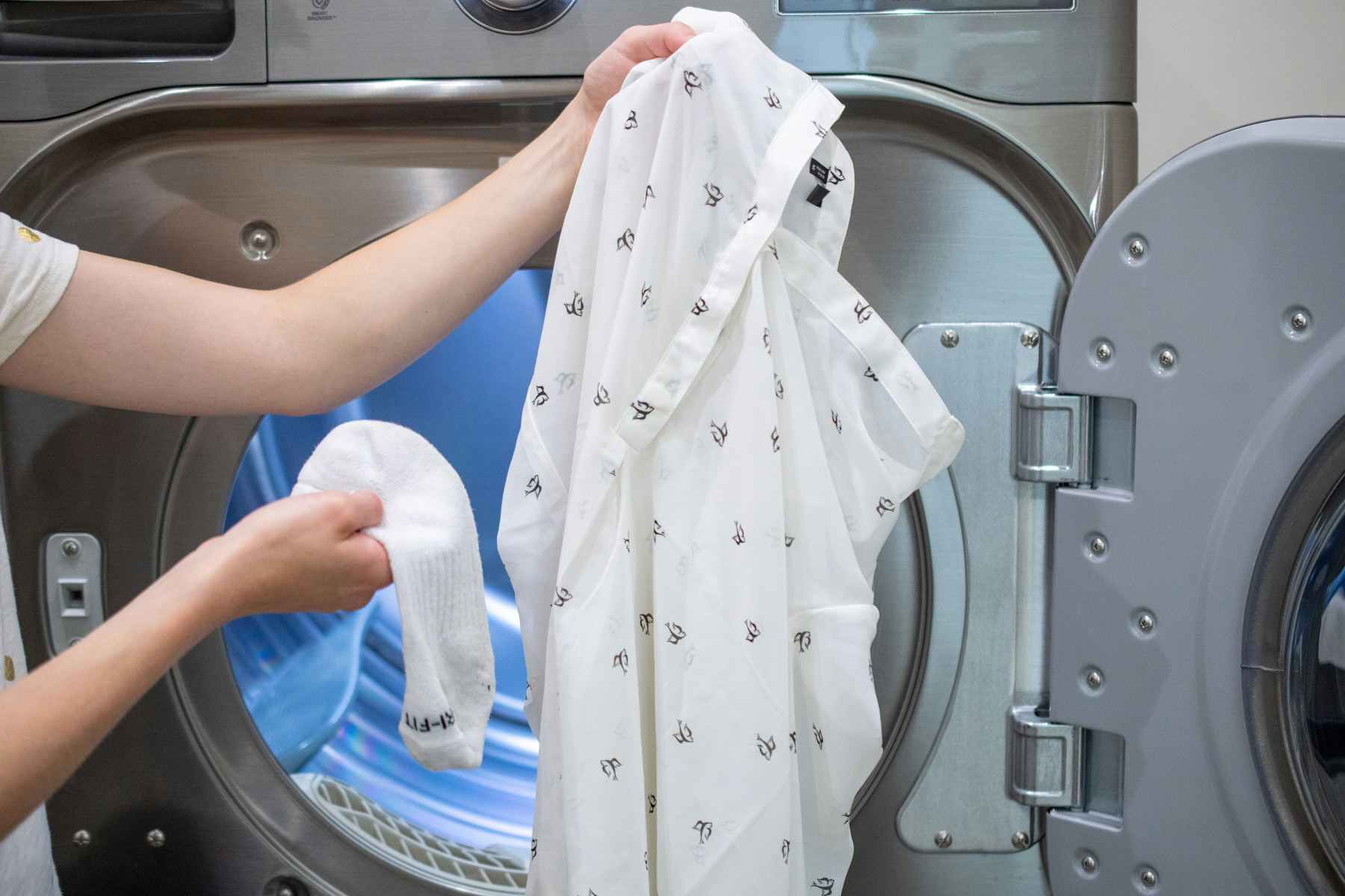 Woman holding a wet sock with a wrinkled shirt in front of a clothes dryer.