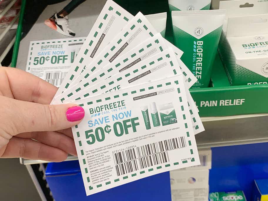 A person holding five coupons for BioFreeze in front of a Biofreeze store display.