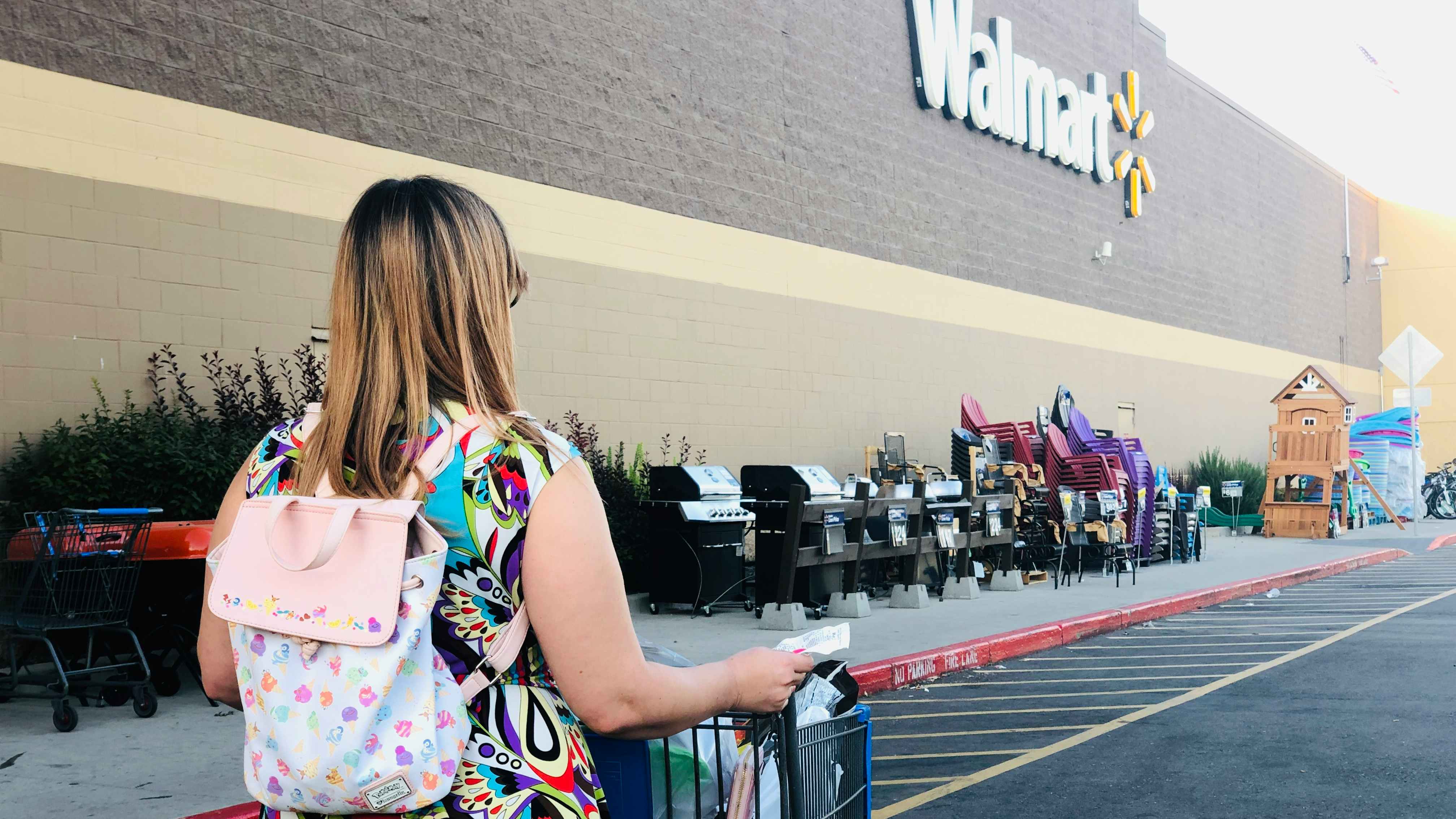 lady wearing backpack pushes cart towards walmart