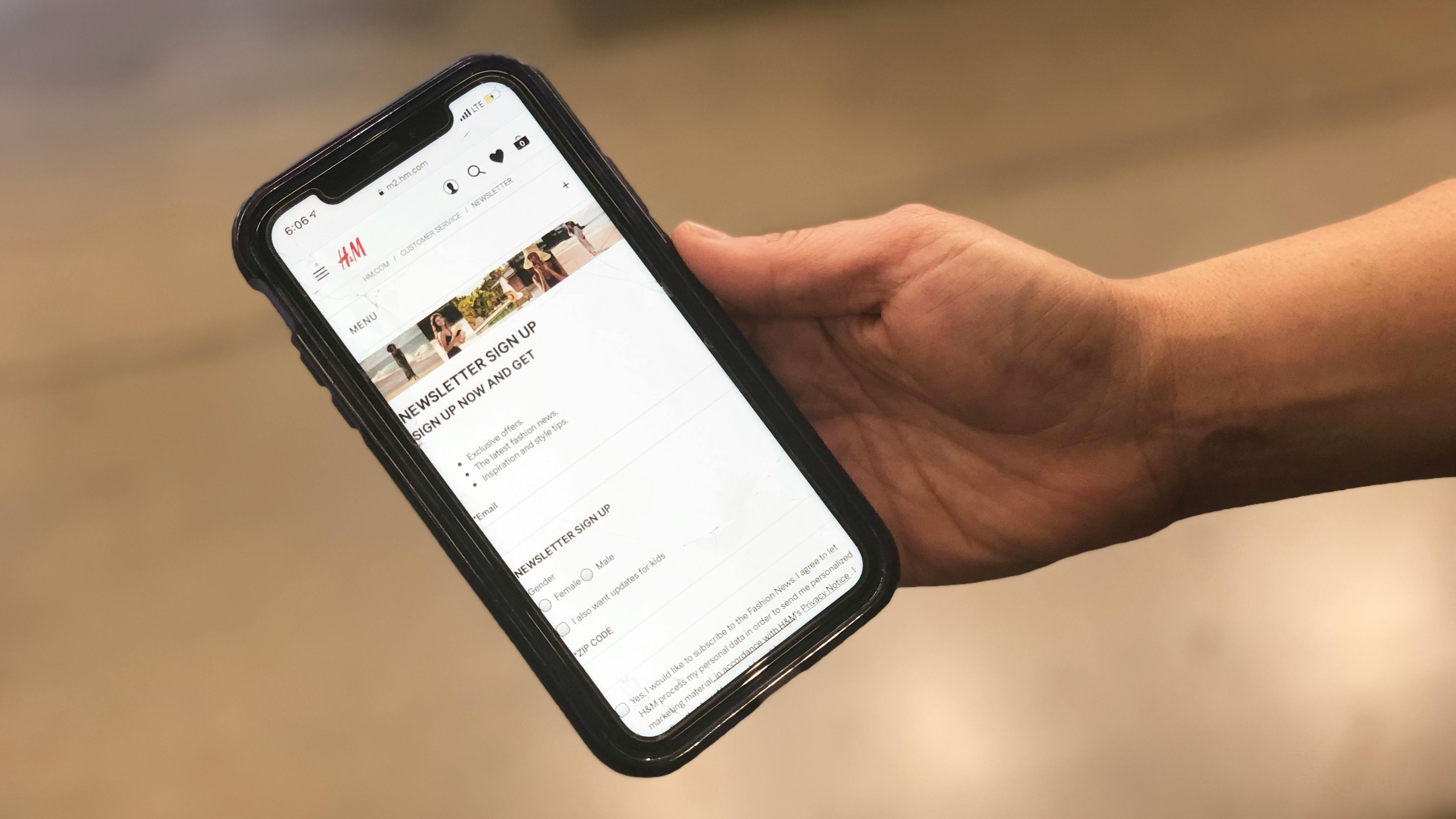 A hand is holding a phone with the HM newsletter sign up