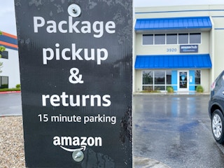 A sign outside an amazon hub location with the warehouse front entrance in the background
