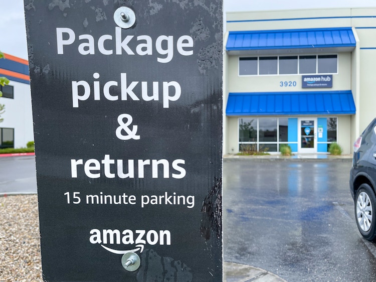 A sign outside an amazon hub location with the warehouse front entrance in the background