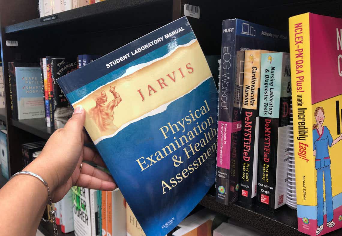 A person pulling a college textbook off a shelf