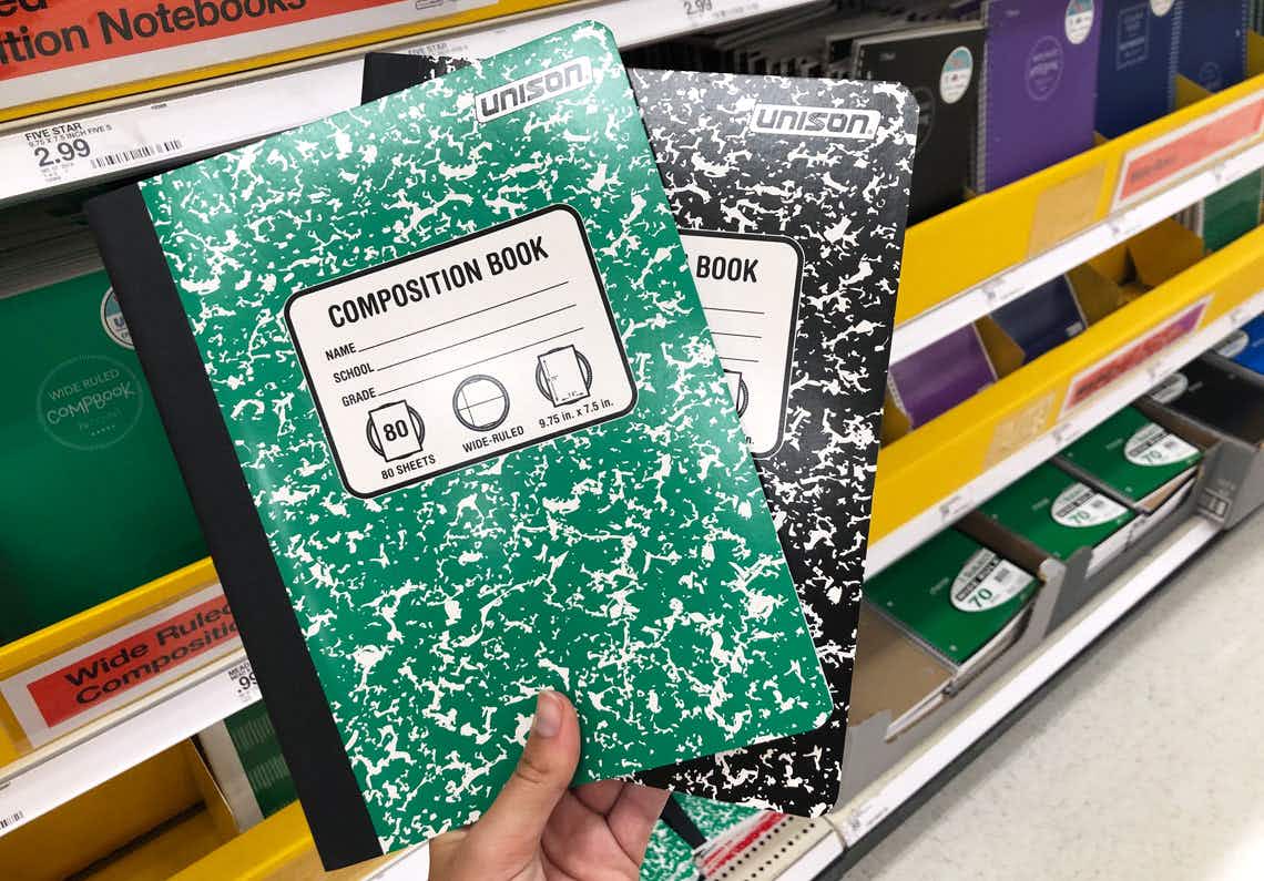 A person's hand holding two Composition notebooks in front of a shelf of notebooks inside Target.