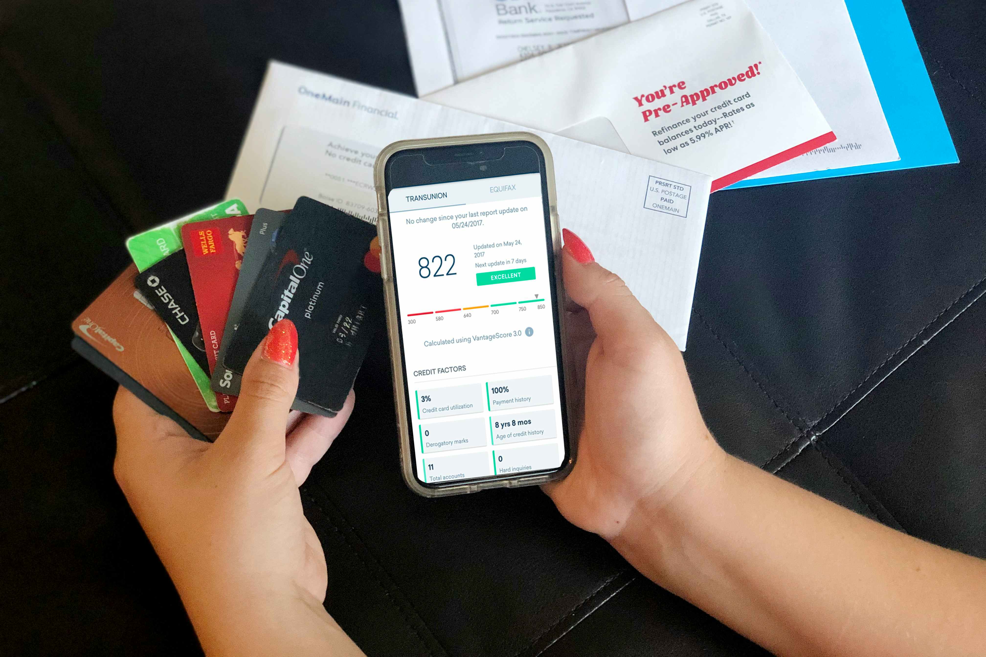 A person holding a cellphone displaying the Credit Karma app and a handful of credit cards