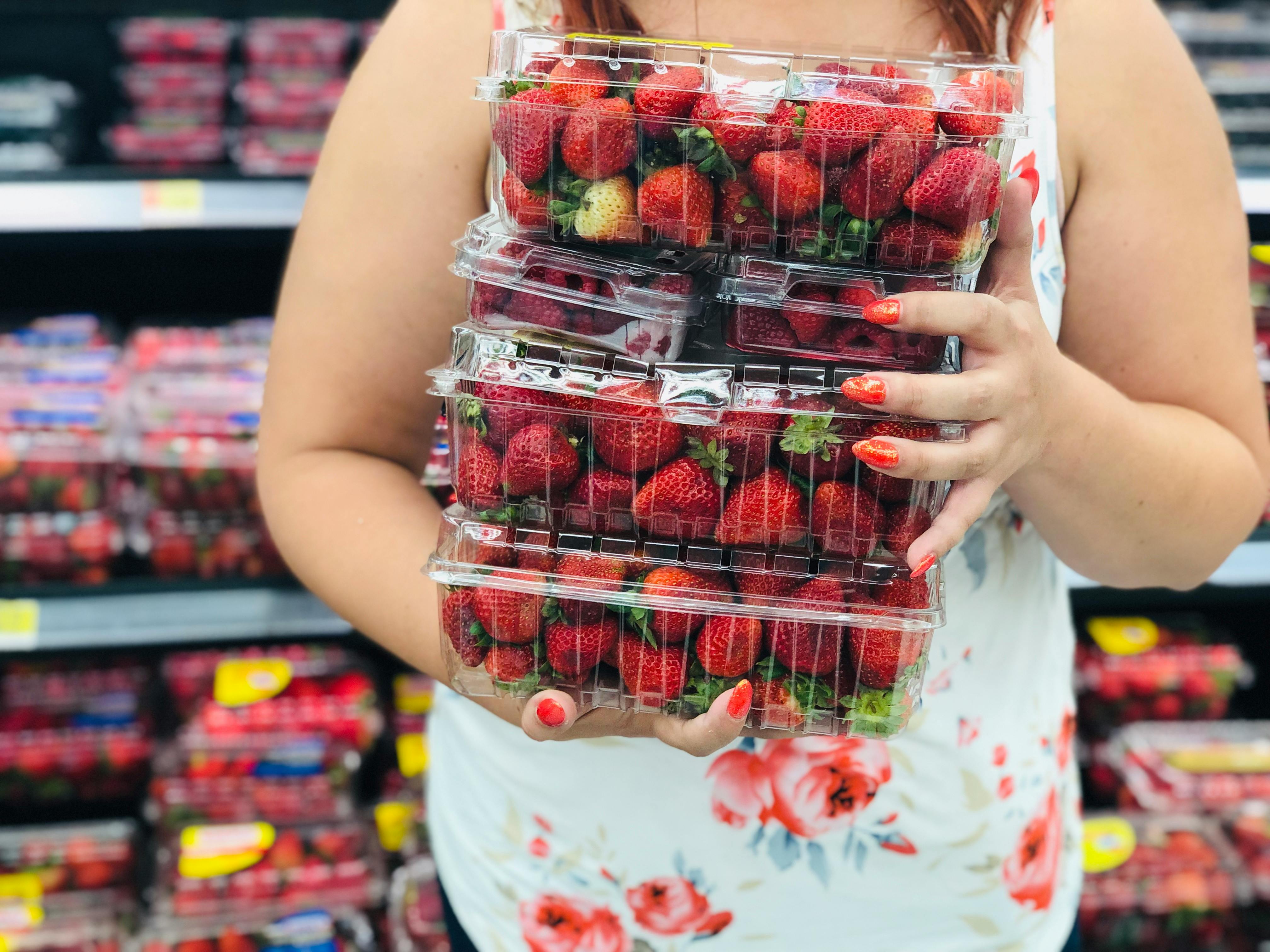 woman holds three large plastic strawberry containers