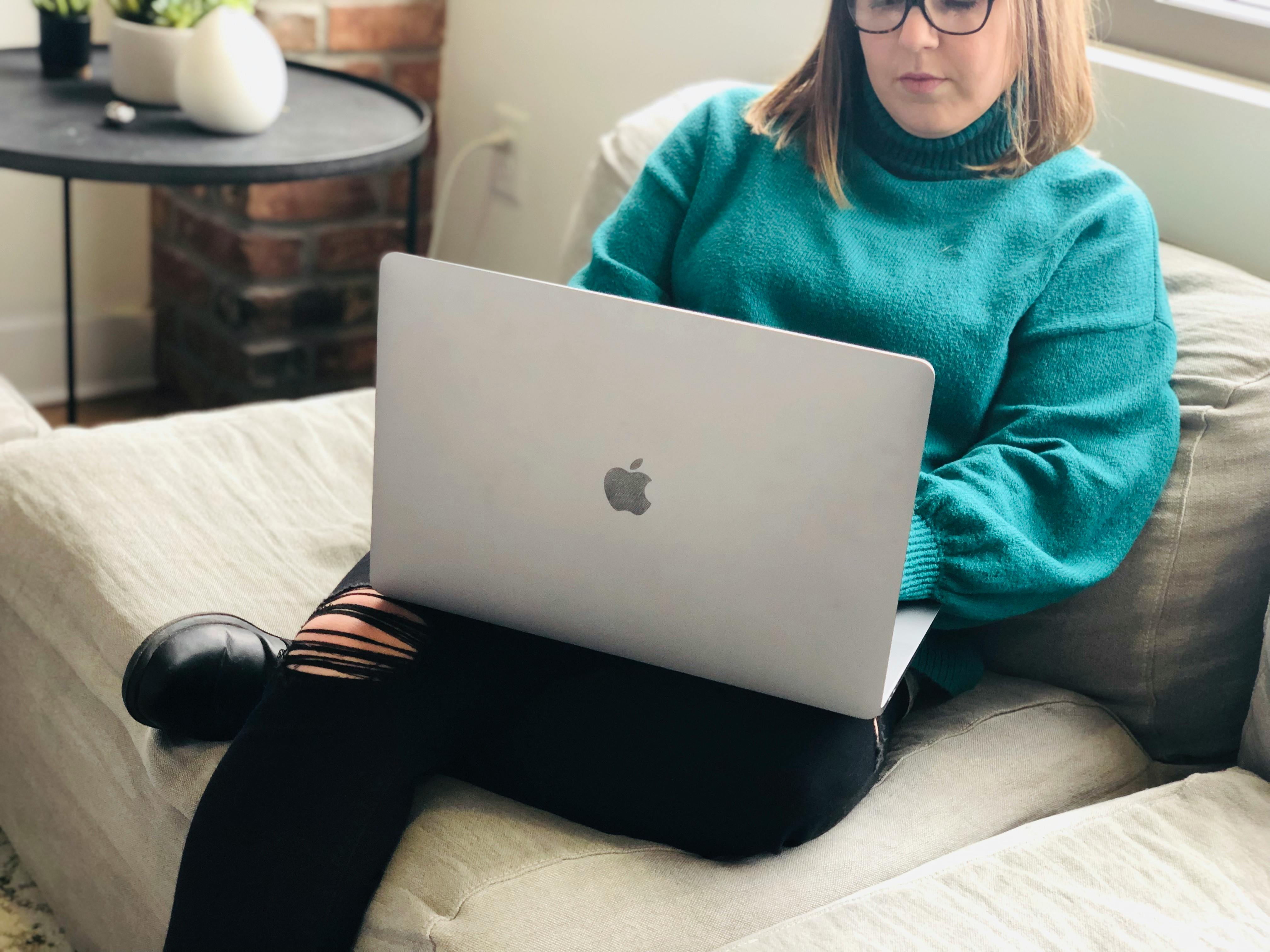 A woman sitting on a couch, working on a macbook computer. 