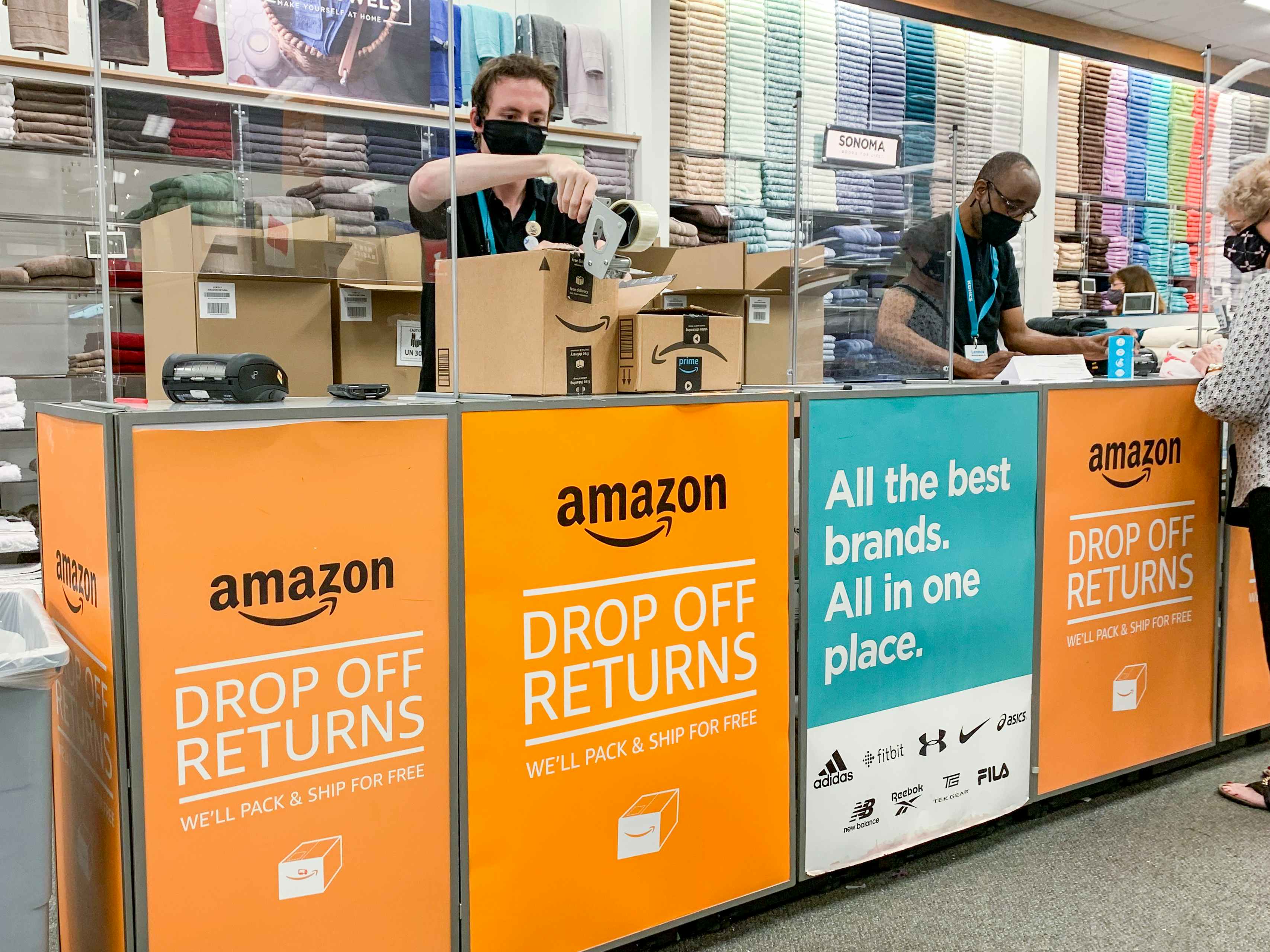 A Kohl's employee taping an Amazon return box at the Amazon Drop Off Returns counter inside Kohl's.