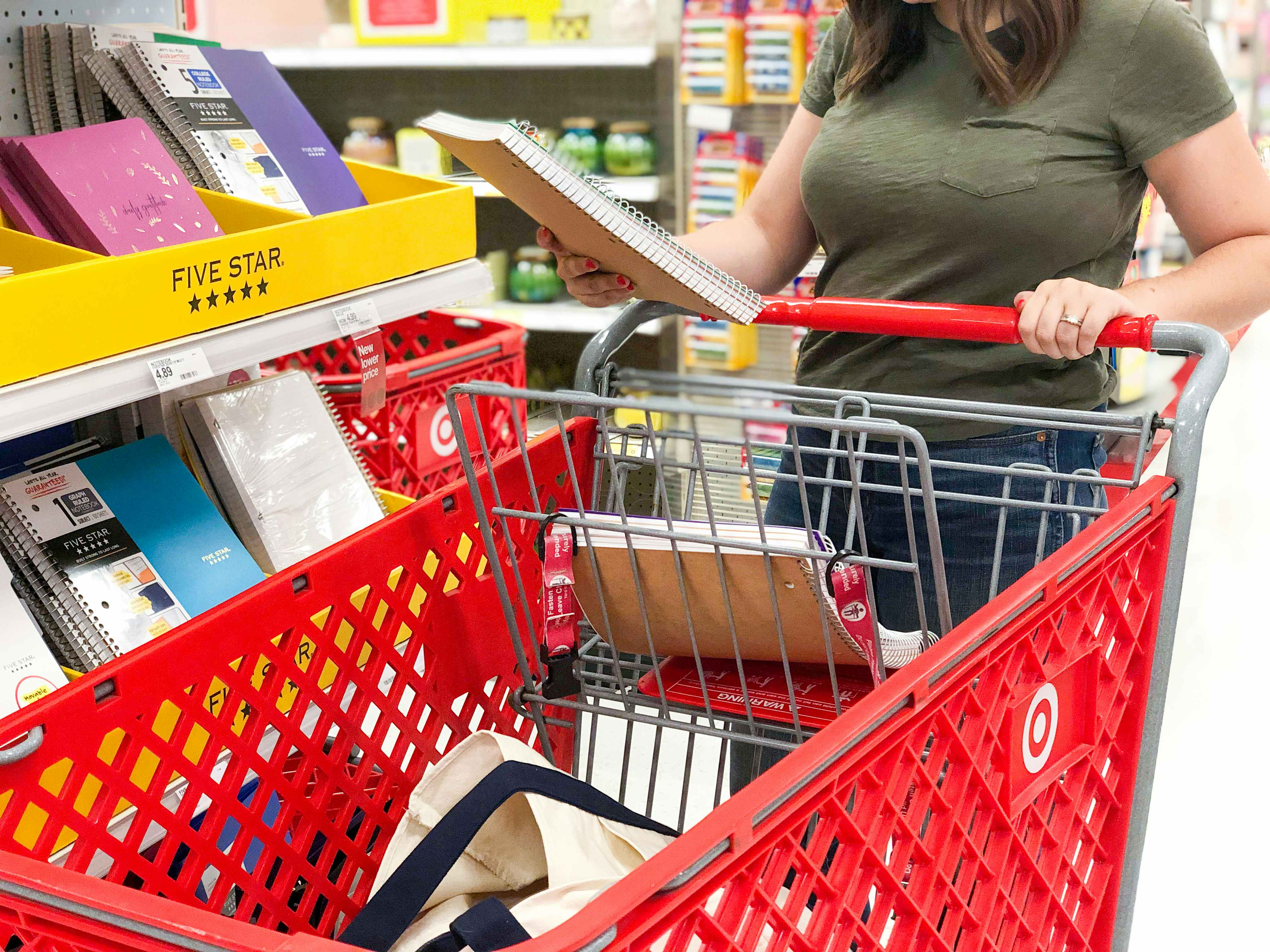 A woman pushing a target shopping cart and holding a five star notebook in her hand
