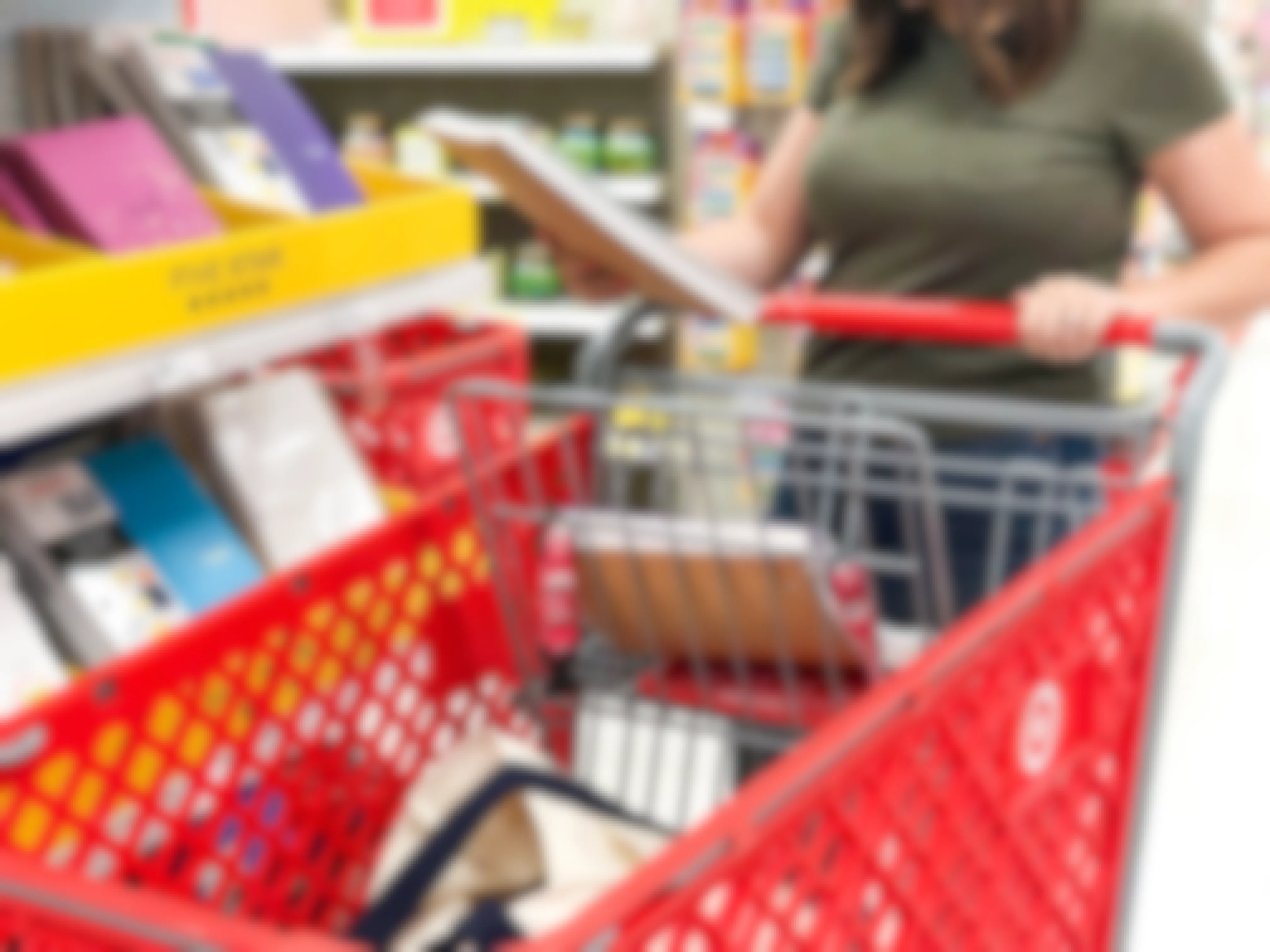 A woman pushing a target shopping cart and holding a five star notebook in her hand