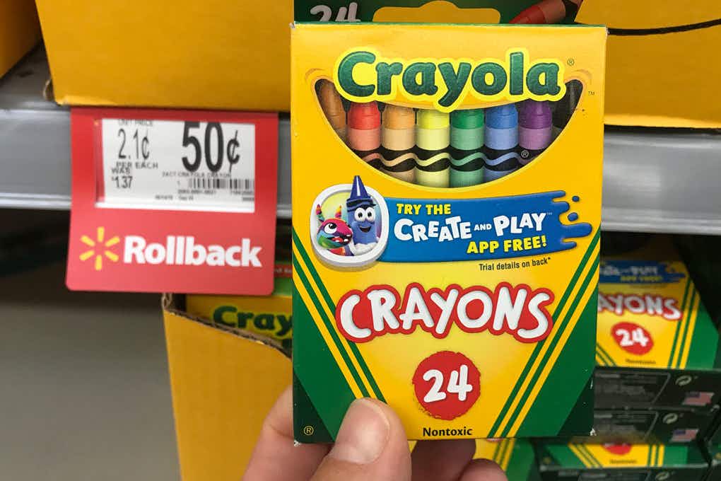A person's hand holding a box of 24 count Crayola crayons next to a Walmart rollback price tag for $0.50