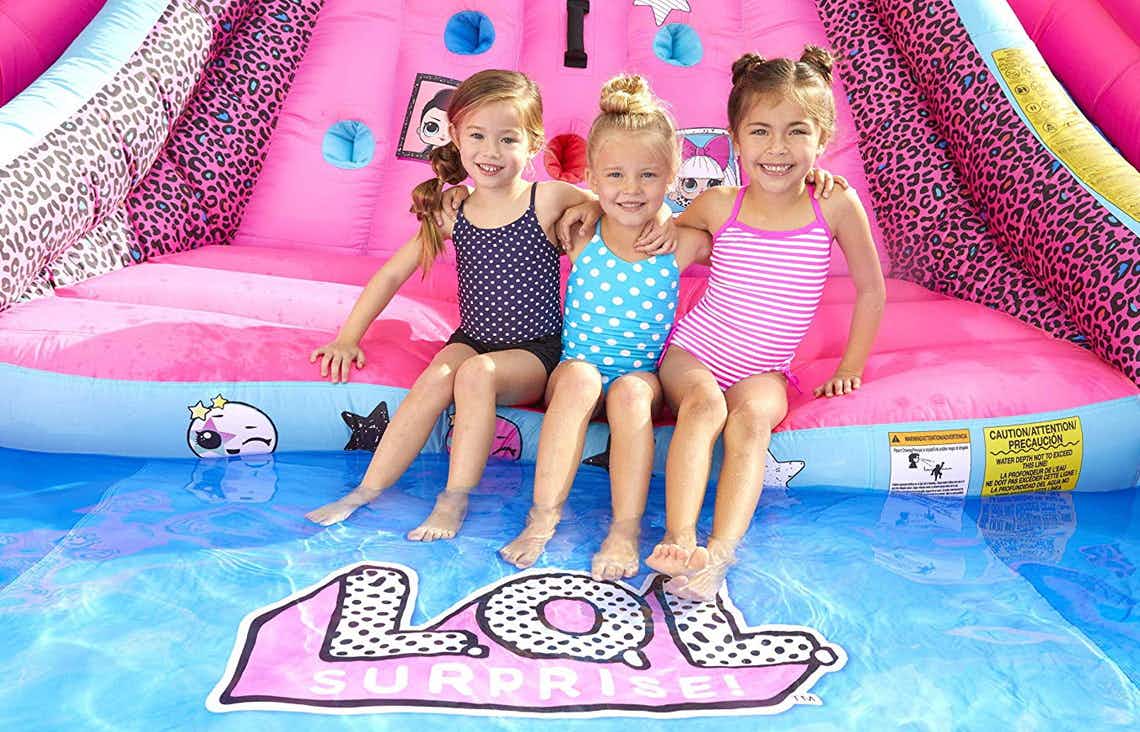 Three young girls sitting on a LOL Surprise water slide