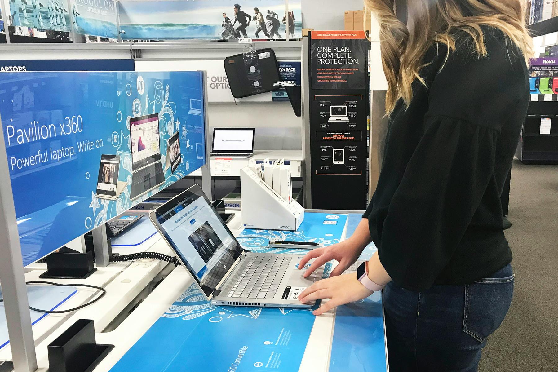 A woman using the touchpad of a display laptop in the computer section at Best Buy.
