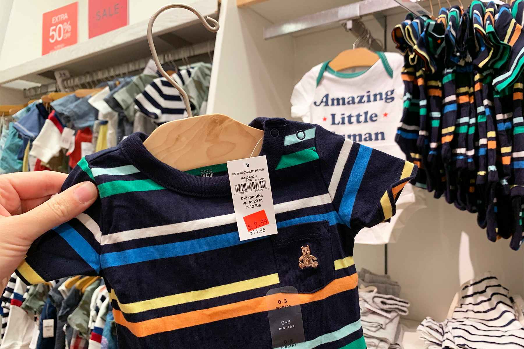 A person holding up a children's t-shirt in front of other kids clothing in the clearance section. 