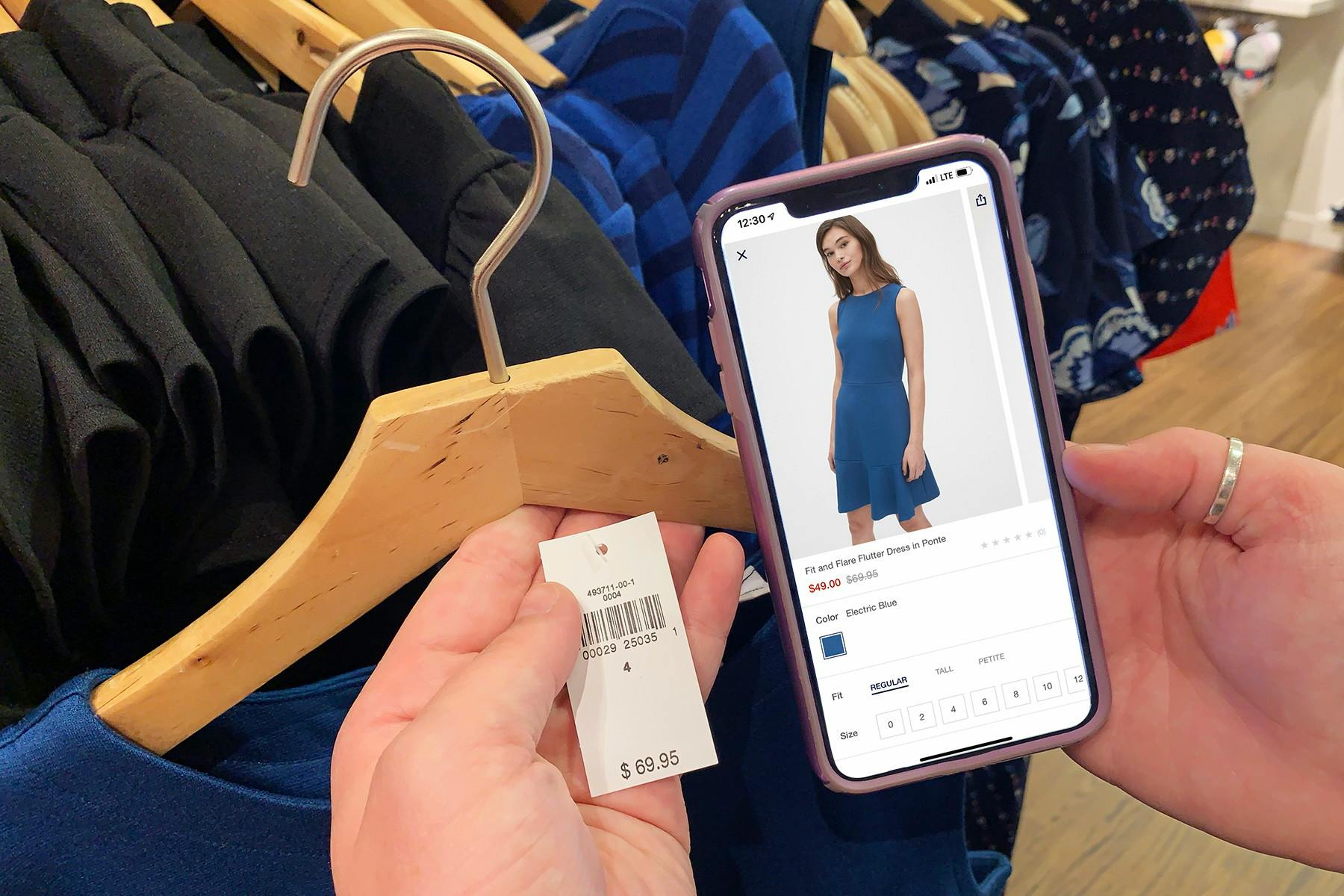 Someone holding up a price tag on a clothing item and comparing it to the same item pulled up on a phone