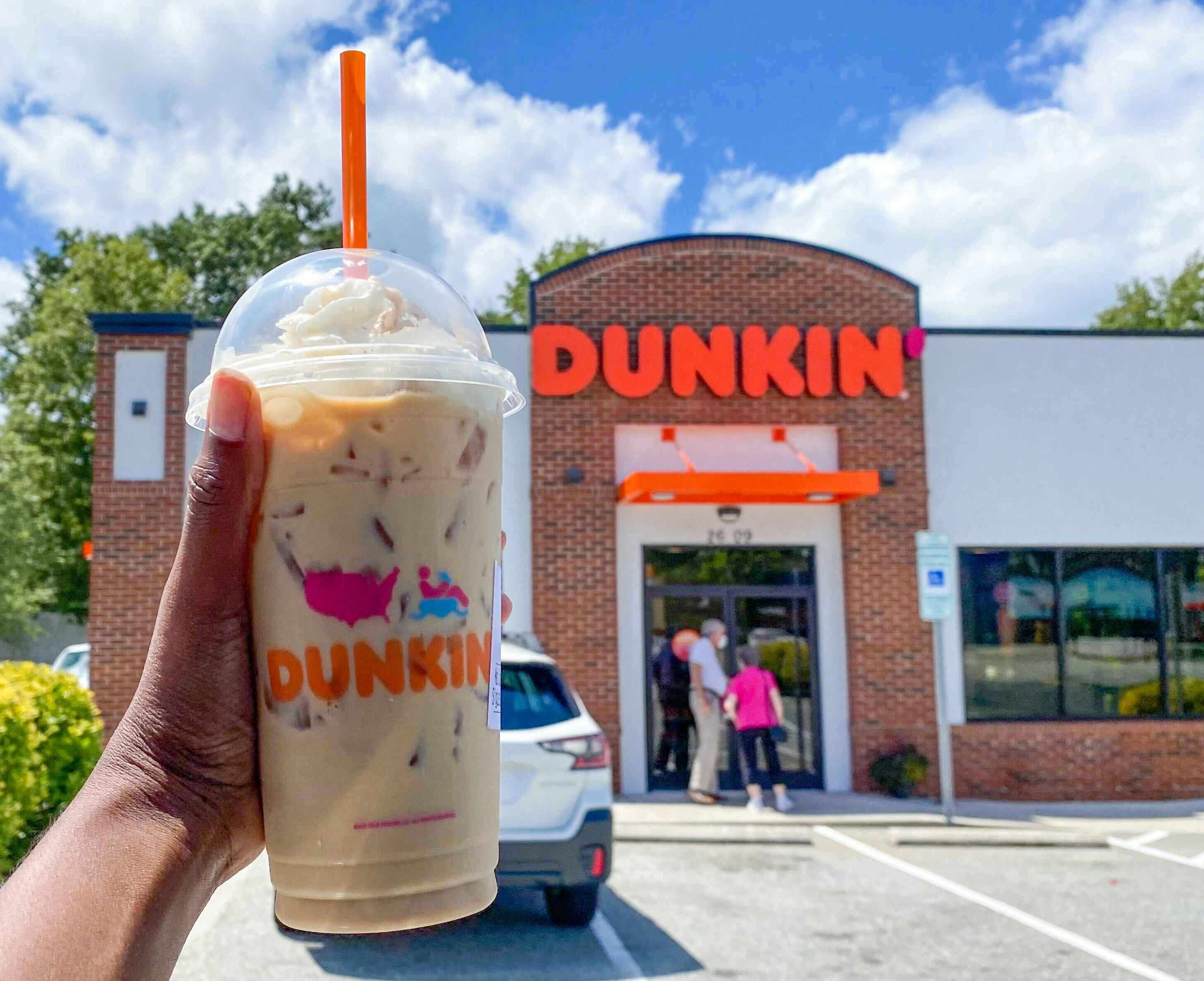 Someone holding the pumpkin spice latte in front of the dunkin' donuts store front.