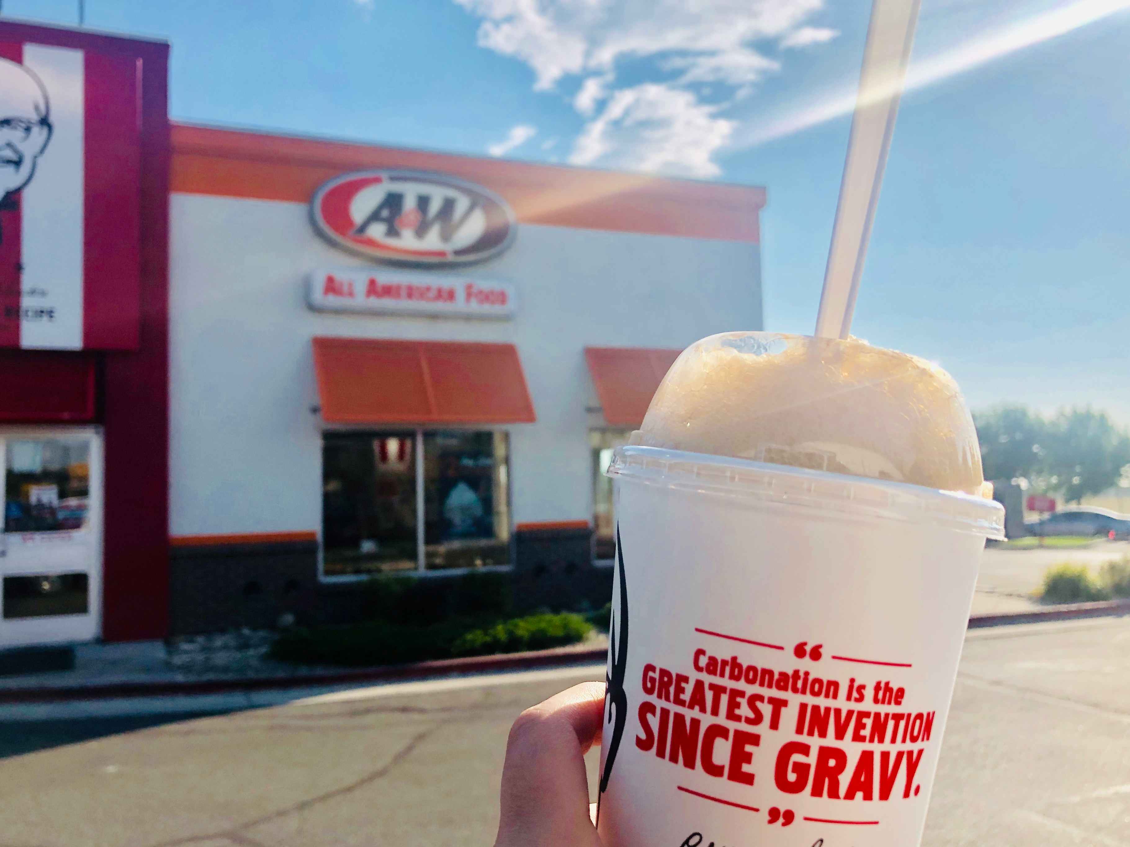 a person holding up a rootbeer float in front of an A&W store