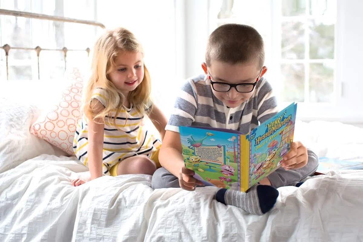 two children reading a book on a bed
