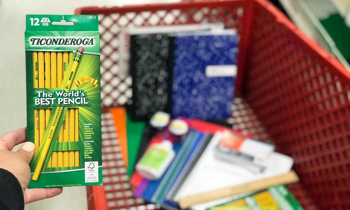 A person's hand holding a box of Ticonderoga pencils above a shopping cart filled with other office and school supplies.