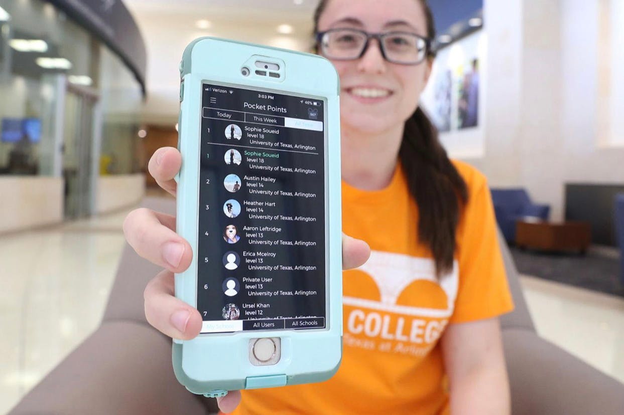 A college student sitting in a chair and holding up a cell phone displaying the Pocket Points app.
