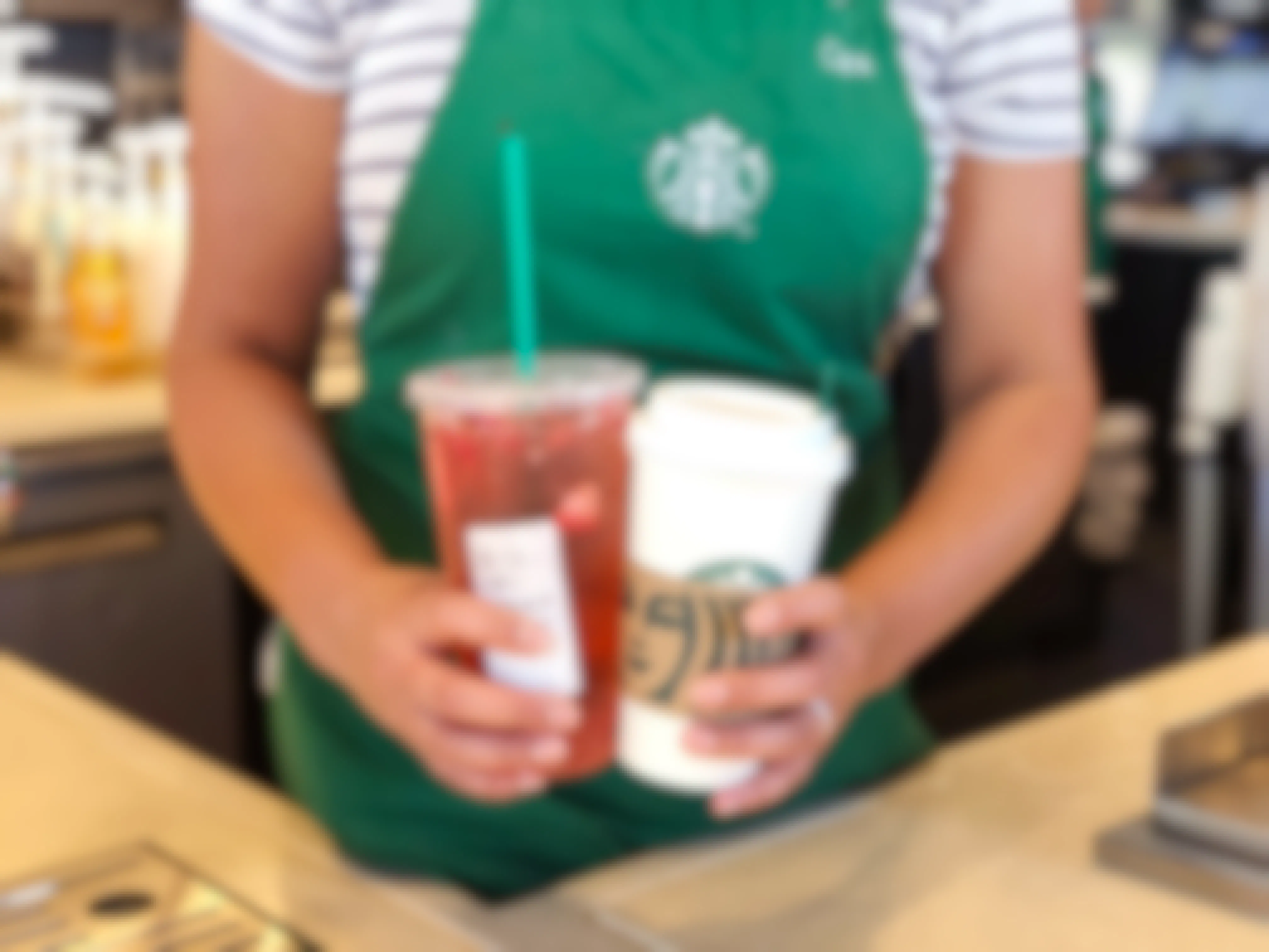 A Starbucks barista holding two Starbucks drinks over the counter.