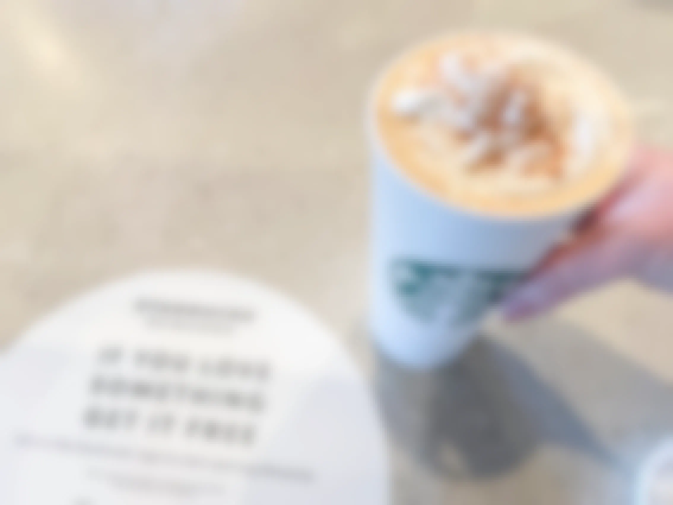 A person holding a Starbucks pumpkin spice latte next to a Starbucks rewards sign.