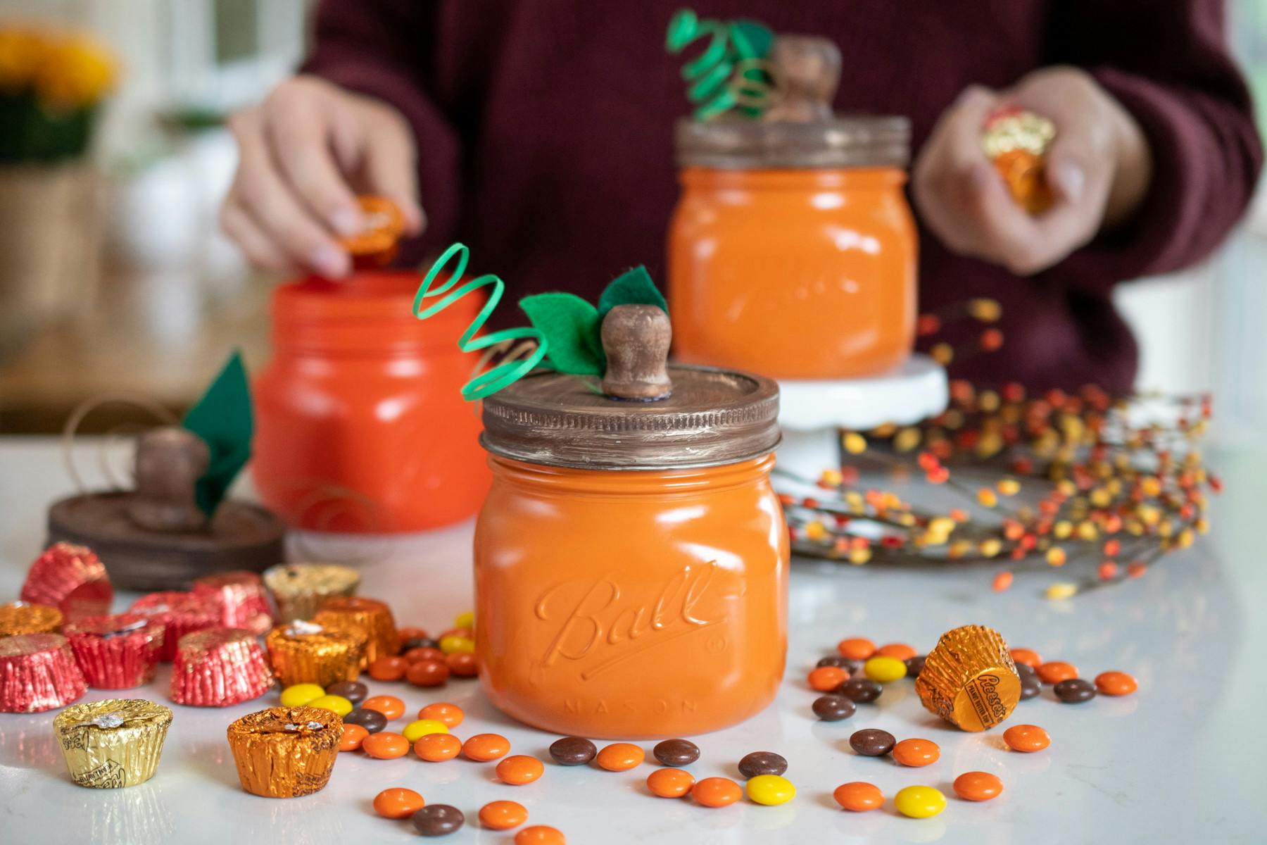 A person putting candy into mason jars that have been decorated to look like pumpkins.
